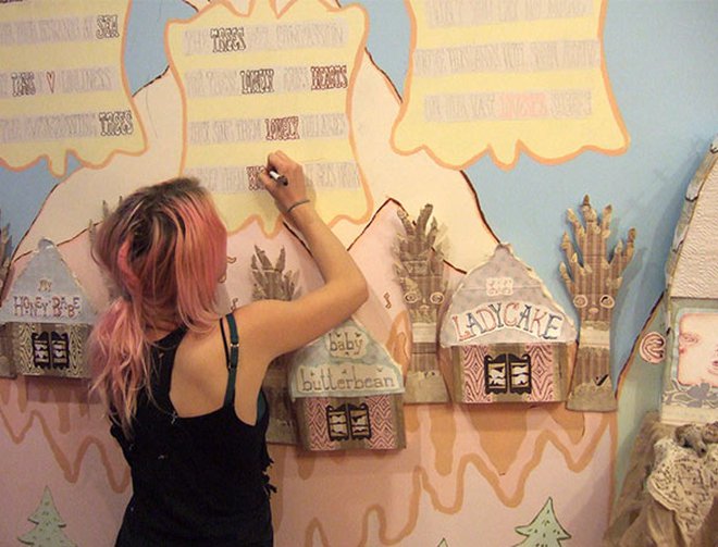 An artist creating a mural which includes store fronts using a marker. 