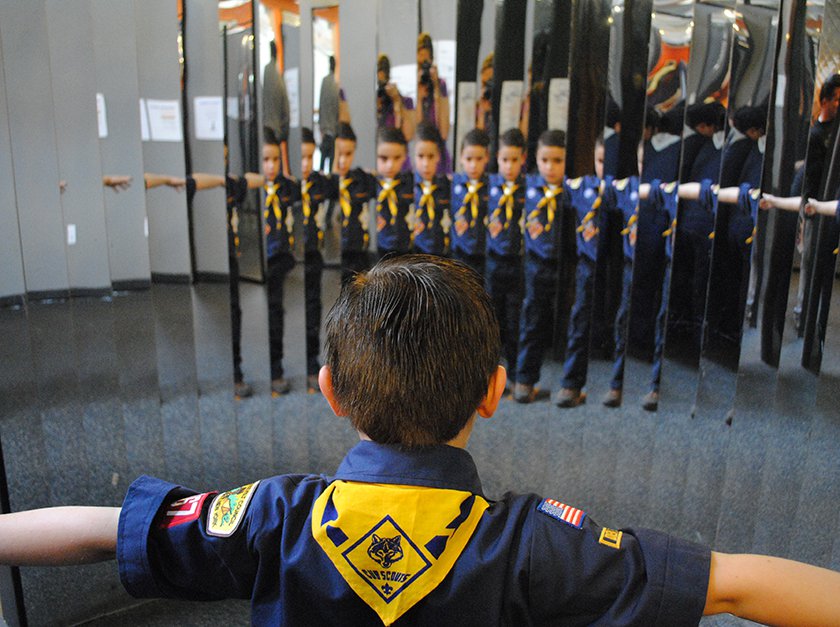 A Boyscout standing in front of the mirror looking at his many reflections. 