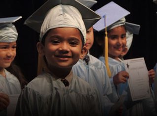 Pre-K program graduate in cap and gown on stage. 