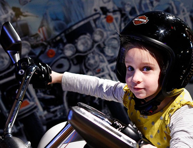 Child sitting on motorcycle wearing a helmet in exhibit. 