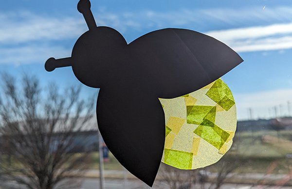 A black paper firefly with a back made from translucent yellow tissue paper. 