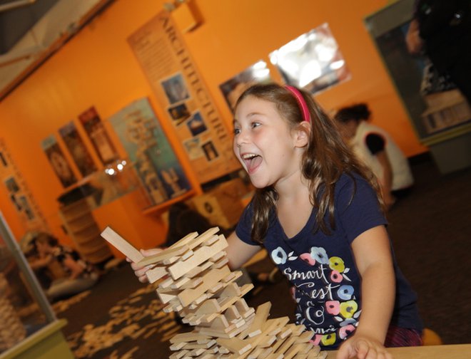 A girl playing with KEVA blanks and building a structure.