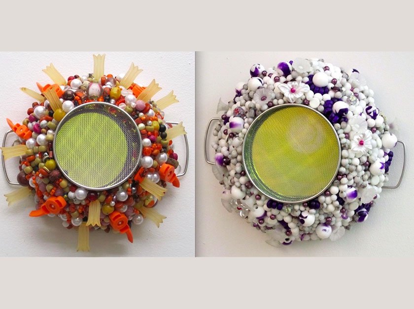 Two metal strainers decorated with various glass beads and rocks. The strainer on the left is decorated with orange, white, green and yellow objects and the strainer on the right is decorated with white and purple objects.