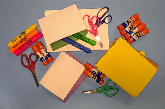 A scattered pile of colored coonstruction paper, markers, scissors and glue sticks. 