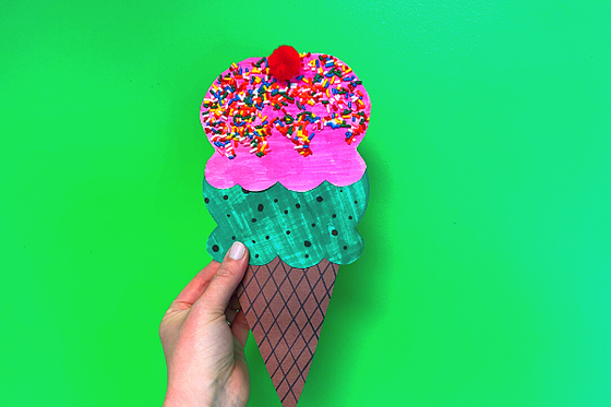 One pink and one green scoop of paper ice cream decorated with sprinkles and a cherry on a cone.  