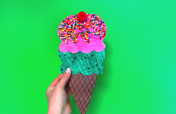 One pink and one green scoop of paper ice cream decorated with sprinkles and a cherry on a cone.  