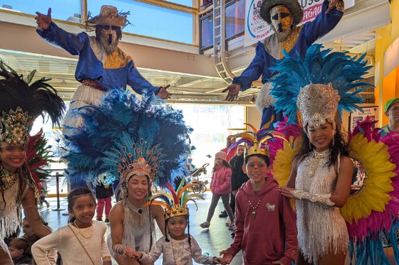 A group of children, two stilt walkers, and dancers. 