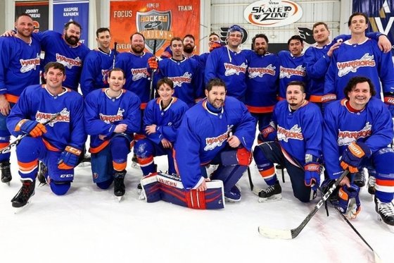 Eighteen hockey players lined up in two rows wearing blue LI Warriors uniforms.