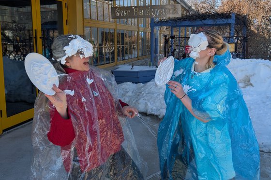 Two women covered in shaving cream laughing. They are wearing ponchos and goggles. 