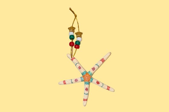 A decorated starfish with a small loop of string and beads on a yellow background.