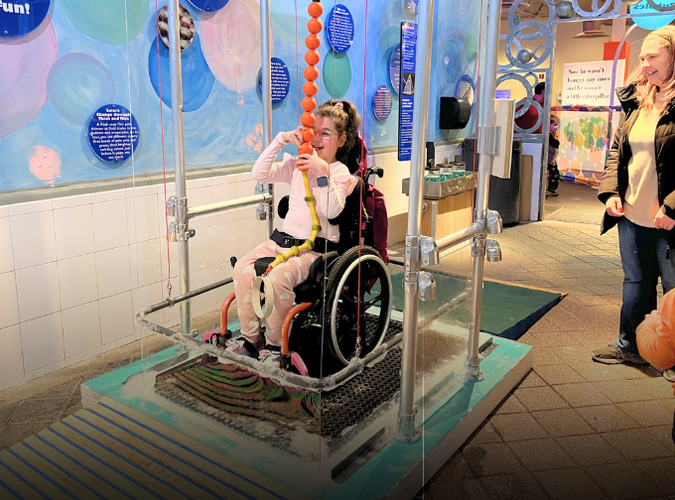 A child in a wheelchair on a platform and pulling the bubble around her using a rope. 