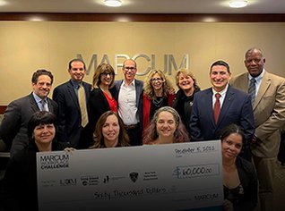 Staff from Marcum and LICM, in professional attire, standing and sitting in front of their logo with a 'giant' donation check. 