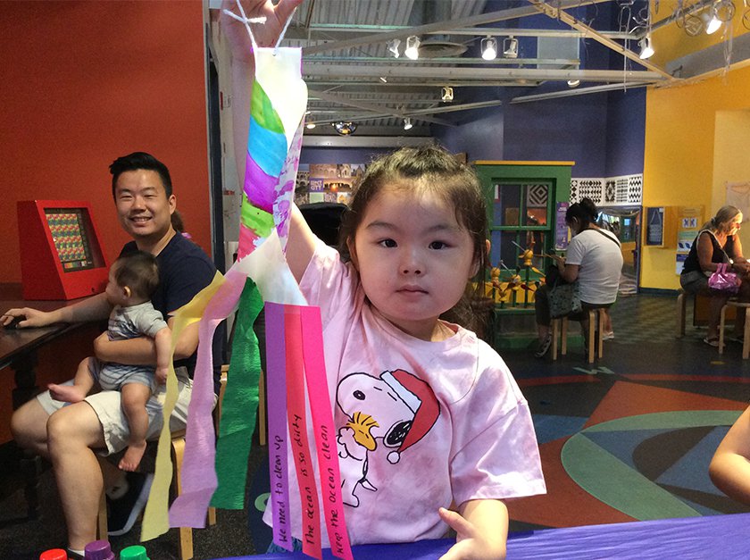 A child holding a colorful paper wind sock shaped like a carpe. 