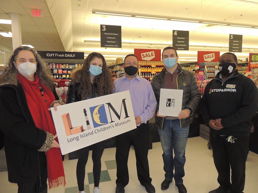 A group of five people standing inside of a grocery store, wearing facemasks, and holding an LICM sign. 
