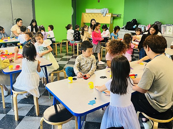Group of children sitting at tables with a teachers while playing with Play Doh. 