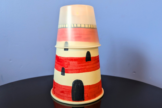 A paper cup decorated like a white and red stripped lighthouse. 