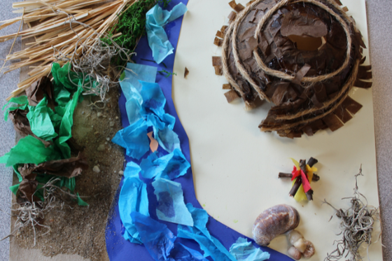 A wigwam made from rope and brown tissue paper, with a landscape of a river, sand, grass, and sticks made with a variety of craft materials.
