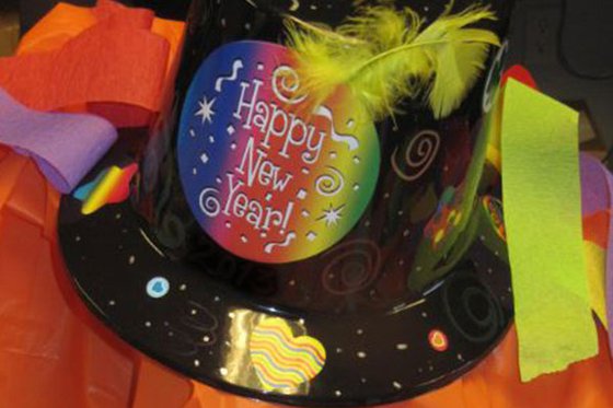A black plastic top hat decorated with streamers, feathers and swirls. The hat reads "Happy New Year." 