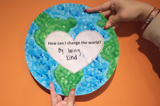 Painted paper globe with a white paper heart in the center with the text "How can I change the world" and "By being kind" written below. 