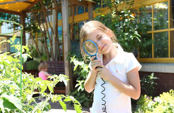 A girl using a magnifying glass to look at a plant in Museum's garden. 