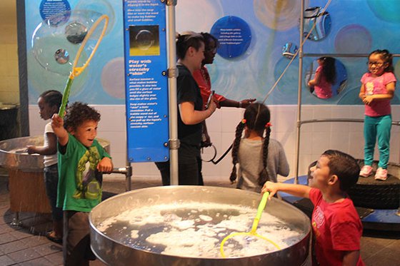 Children playing in Bubbles exhibit with two aduts. 
