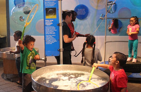 Children playing in Bubbles exhibit with two aduts. 