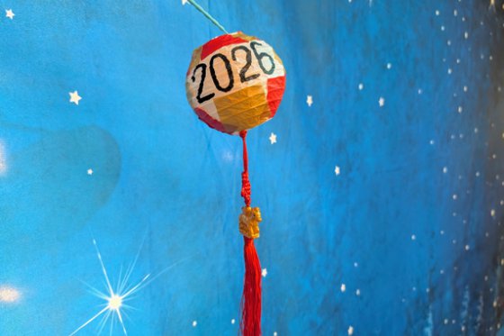 Red, white, and gold paper lantern with "2026" written in black, with a red tassel and gold horse charm attached.