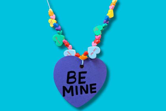 A necklace with colorful round and heart-shaped beads with text "luv you" and one large heart paper pendent with text "Be Mine." 