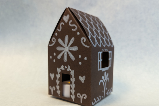 A gingerbread house made with brown paper and decorated with a white marker. 
