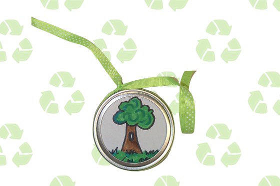 A metal lid decorated with a drawing of a tree and grass and a green ribbon against a graphic of green recycling symbols. 