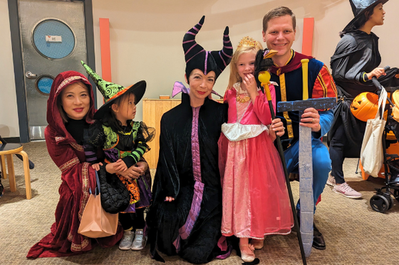 Two children in Disney costumes standing while their adults kneel around them in Disney costumes. 