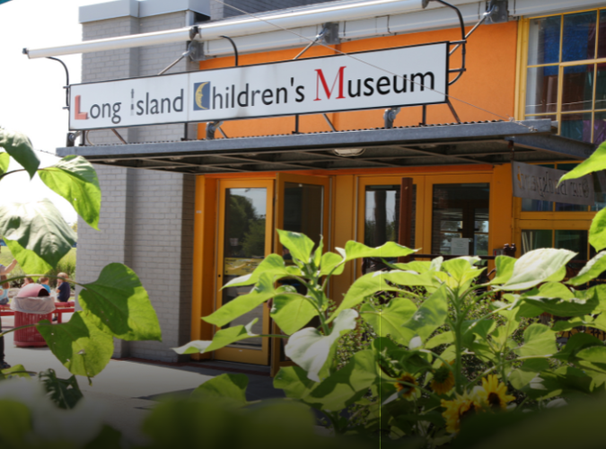 The East entrance of the Long Island Children's Museum with sunflowers and leaves in the foreground.