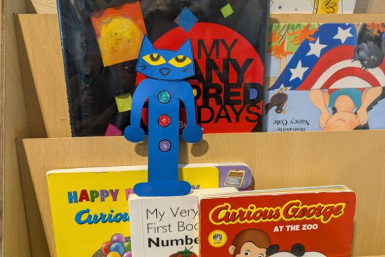 Blue Pete the Cat in the shape of a bookmark, laid against books on a shelf. 