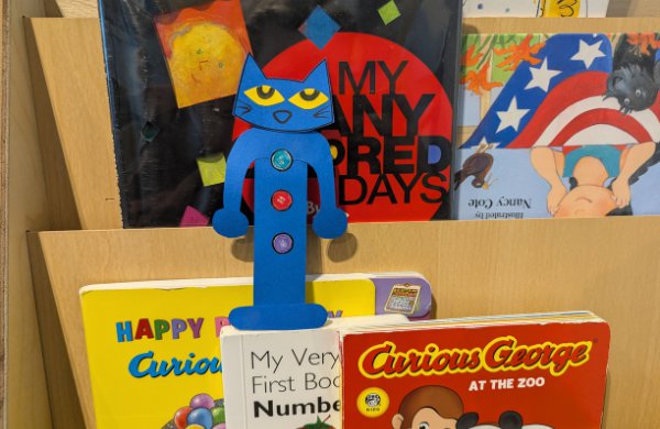 Blue Pete the Cat in the shape of a bookmark, laid against books on a shelf. 