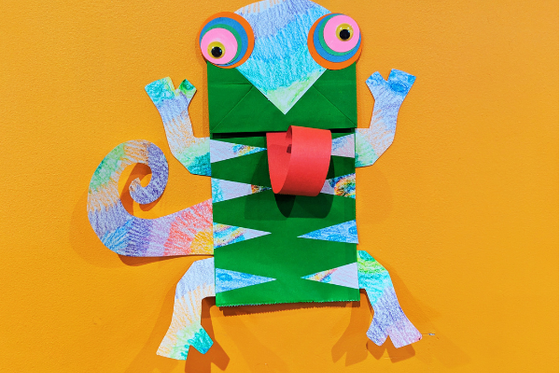 A colorful chameleon made with a brown paper bag and a long, red curled tongue. 