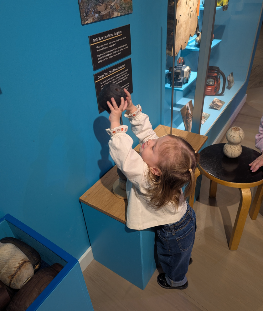 A toddler reaching to stack round wooden blocks on a rod. 