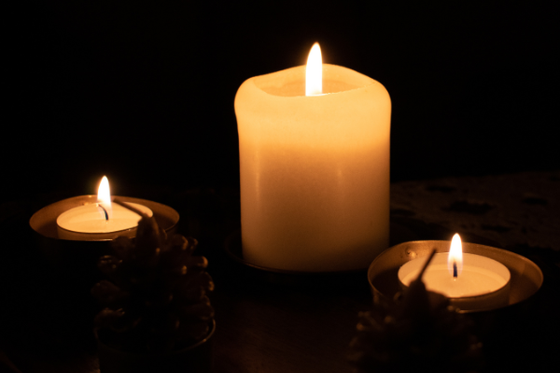Three lit candles in metal containers surround by pinecones. 