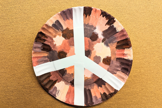 Peace sign on a paper plate decorated with a variety of skin tone colored dots. 