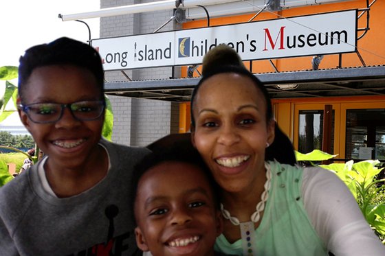 An adult woman and two children using the Zoom background of the exterior of LICM. 