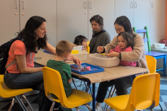 A group of children and adults sitting together at a table doing sensory play. 