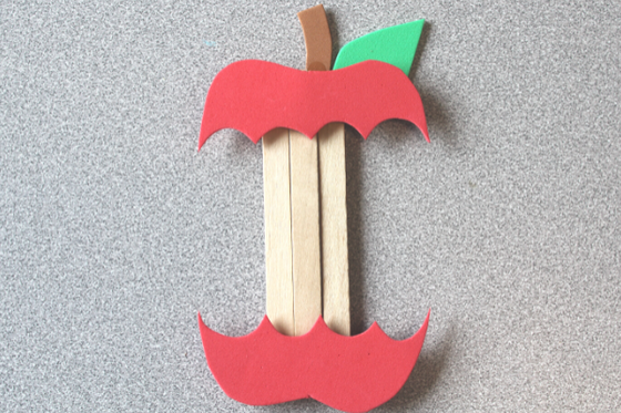 A red apple made from foam with a large bite taken out to create a popsicle stick core. 