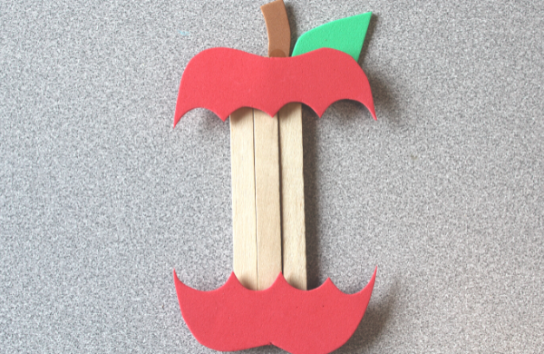 A red apple made from foam with a large bite taken out to create a popsicle stick core. 