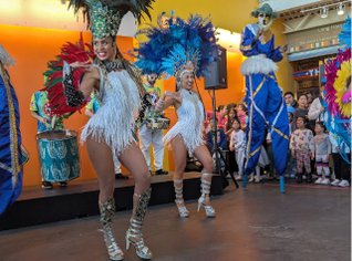 A group of children, two stilt walkers, and dancers in celebratory dress.