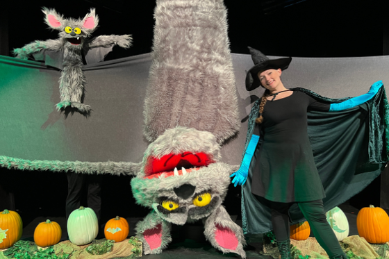 A small puppet of a bat, a large puppet of a bat, and a witch on LICM's theater stage.