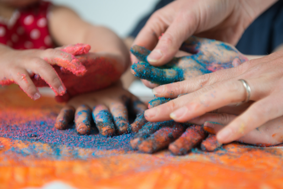 Adult and children hands playing with colored sand. 