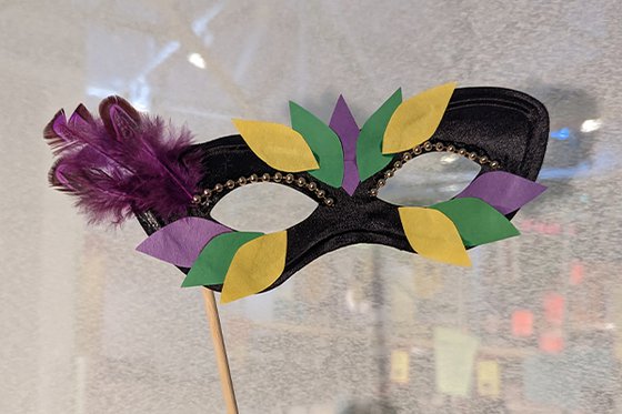 Black domino mask decorated with purple, yellow and green feathers. 