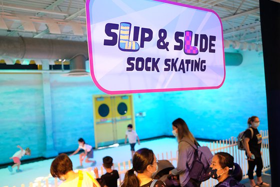 Entrance to exhibit "Sock Skating" featuring multiple adults watching children slide on the white floor while wearing face masks. 