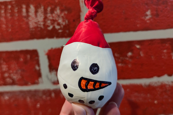 A defalted upside balloon painted white with a snowperson's face. 