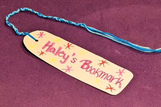 A handmade bookmark decorated with text Haley's Bookmark and yarn. 