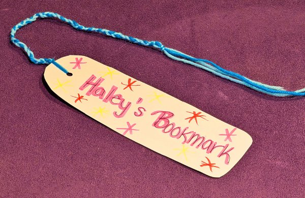A handmade bookmark decorated with text Haley's Bookmark and yarn. 